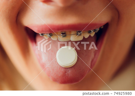 Taking pills. Woman taking pill - closeup of tongue. 74925980