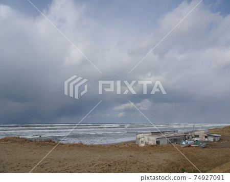 A landscape of the Sea of Japan in winter with a sandy beach with a hut and a fishing boat and a winter sky 74927091