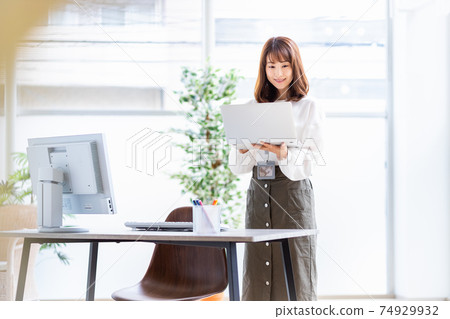 A woman standing with her laptop open in a bright room A woman standing with her laptop open in a bright room 74929932