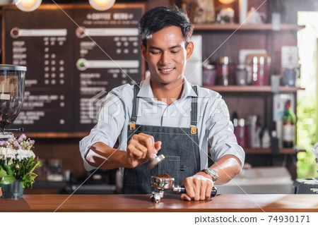 Asian Barista tamping the portafilter and preparing cup of coffee, espresso with latte or cappuccino for customer order in coffee shop, Small business owner and startup in coffee shop concept 74930171