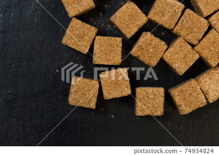 Cane sugar cubes, top view. Black background. Brown sugar texture Cane sugar cubes, top view. Black background. Brown sugar texture 74934824
