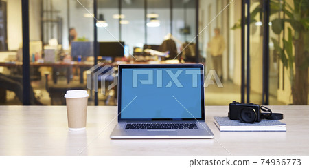 a laptop computer with blue screen, together with a camera and a cup of coffee on desk in a small stylish office. 74936773