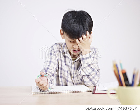 10 year-old asian elementary schoolboy appears to be frustrated while doing homework. 10 year-old asian elementary schoolboy appears to be frustrated while doing homework. 74937517