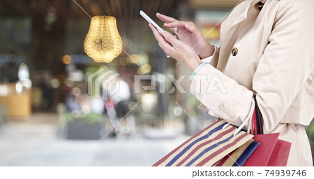 hands of a young woman using mobile phone while walking in shopping district 74939746