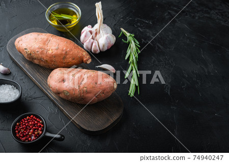 Raw whole sweet potatoe with herbs and spices on black background with copyspace 74940247