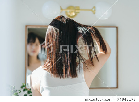 A woman with her hair fluttering in front of a mirror A woman with her hair fluttering in front of a mirror 74942175
