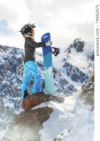 Portrait of active female snowboarder in funny hat standing on top of the mountain background. Portrait of active female snowboarder in funny hat standing on top of the mountain background. 74942671