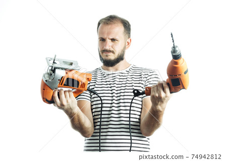 How to choose a power tool. Portrait of bearded handyman holding orange drill and electric jigsaw isolated on white 74942812