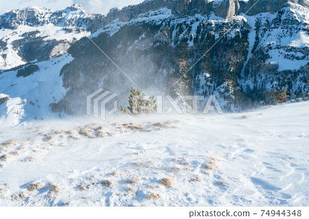 Blowing snow over snowy surface on top of mountain in Switzerland - snowstorm 74944348