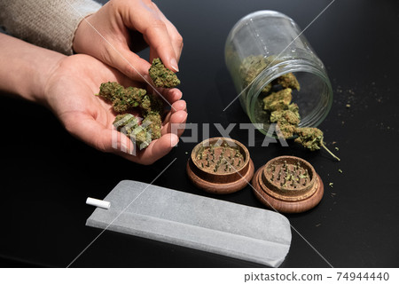 Cannabis buds in a hand and other smoking utensils on a table 74944440