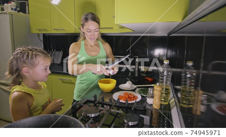 Mother teaching daughter smart girl learning to cook. Mistress children to cook a Neapolitan egg fried omelette from salame affumicato sausage. Mother teaching daughter smart girl learning to cook. Mistress children to cook a Neapolitan egg fried omelette from salame affumicato sausage. 74945971