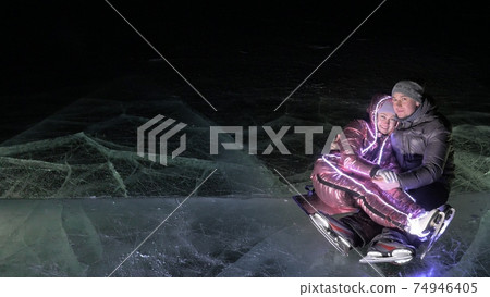 Young loving couple skating at ice rink at night. Man and woman kiss hug have fun learn to skate. Making love on ice. Ice illuminated backlit below. Young loving couple skating at ice rink at night. Man and woman kiss hug have fun learn to skate. Making love on ice. Ice illuminated backlit below. 74946405