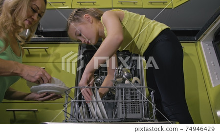 Mother teaching daughter smart girl learning to use dishwasher. Young mistress children loading putting dirty dishes in automatic dishwasher. 74946429