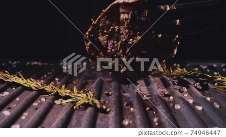 Delicious juicy meat steak cooking on grill. Aged prime rare roast grilling marble beef. Electric roaster, rosemary black pepper, salt. Kitchen tongs. 74946447