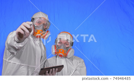 Scientist virologist in respirator makes write in an tablet computer with stylus. Man and woman wearing protective medical mask. Chroma key blue. 74946485