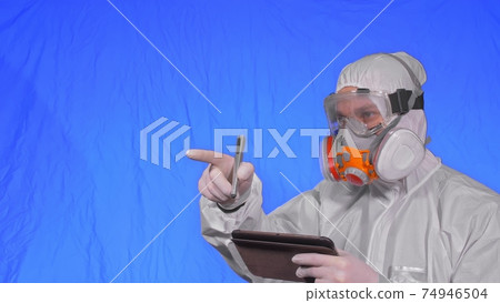 Scientist virologist in respirator makes write in an tablet computer with stylus. Man wearing protective medical mask. Chroma key blue. 74946504