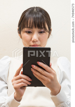Woman sitting on the couch and holding a tablet Woman sitting on the couch and holding a tablet 74946573