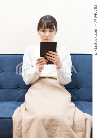 Woman sitting on the couch and holding a tablet Woman sitting on the couch and holding a tablet 74946582