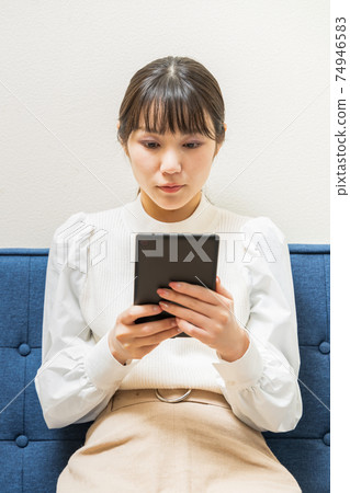 Woman sitting on the couch and holding a tablet Woman sitting on the couch and holding a tablet 74946583