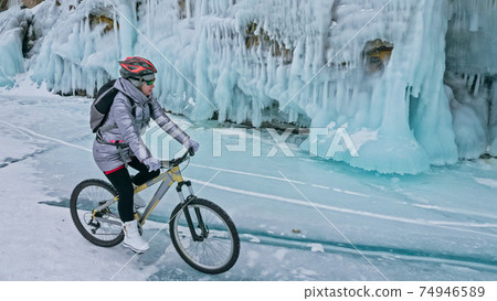 Woman is riding bicycle near the ice grotto. The rock with ice c 74946589
