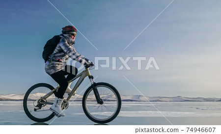 Woman is riding bicycle on the ice. Tires on bike are covered wi Woman is riding bicycle on the ice. Tires on bike are covered wi 74946607