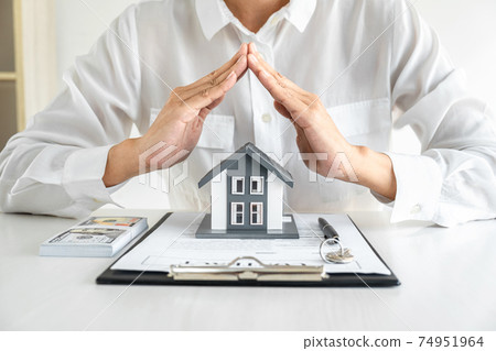Insurance and care protection of house concept, businessman estate agent with protective gesture of small home model by hands 74951964