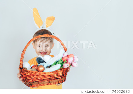 A little boy in a rabbit costume holding a large basket filled with eggs and tulips against a white background A little boy in a rabbit costume holding a large basket filled with eggs and tulips against a white background 74952683