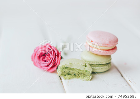 On a wooden background there are two macarons, one green and the other pink, and a beautiful rose with a half macaroon in front of a white background 74952685