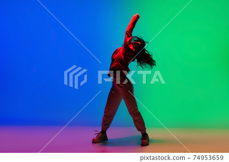 Stylish sportive girl dancing hip-hop in stylish clothes on colorful background at dance hall in neon light. Youth culture, movement, style and fashion, action. 74953659