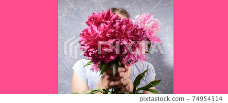 Creative festive banner with faceless young woman in grey T-shirt on grey holding pink peonies in her hands. Trendy style without face. Mother's day or Women holiday. Copy space on magenta backdrop. 74954514