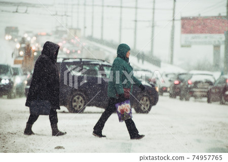 people crossing the road in stormy snowy weather at shallow depth of field 74957765