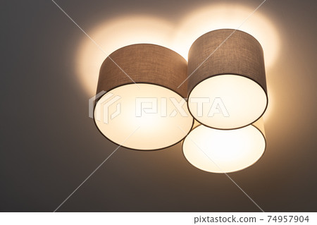 A modern trendy ceiling lamp composed of a group of three cylinders, it shines with warm light. Interior decor details concept, lighting equipment. Scandinavian style. Horizontal A modern trendy ceiling lamp composed of a group of three cylinders, it shines with warm light. Interior decor details concept, lighting equipment. Scandinavian style. Horizontal 74957904