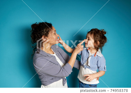 Smiling woman and her child touching each other's nose on blue background with copy space Smiling woman and her child touching each other's nose on blue background with copy space 74958378