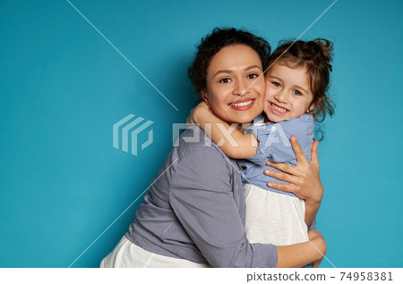 Cheerful mother hugging her daughter. Blue background, happy mother's day concept, Children protection day Cheerful mother hugging her daughter. Blue background, happy mother's day concept, Children protection day 74958381