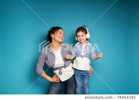 Happy woman lovingly looks at her little daughter in headphones. The concept of the relationship between mother and child. Happy woman lovingly looks at her little daughter in headphones. The concept of the relationship between mother and child. 74958392