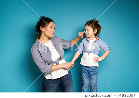 Smiling woman touching her adorable daughter's nose on blue background with copy space Smiling woman touching her adorable daughter's nose on blue background with copy space 74958397