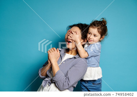 Cute girl hugs her mother covering her eyes with her hands. Emotions. play. love, care, tenderness, happy childhood concept. Cute girl hugs her mother covering her eyes with her hands. Emotions. play. love, care, tenderness, happy childhood concept. 74958402