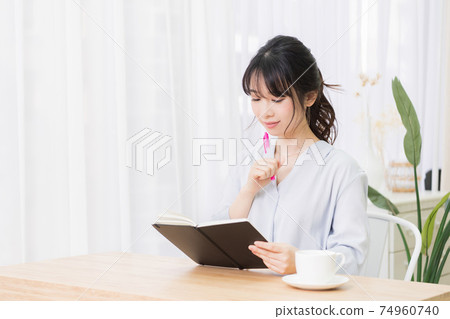 Young woman writing notes in notebook in room Young woman writing notes in notebook in room 74960740
