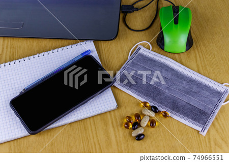 Laptop with mouse, smartphone, notebook, pen, medical mask and vitamins on a desk. Top view. Concept of homeschooling and working from home during quarantine. Stay at home Laptop with mouse, smartphone, notebook, pen, medical mask and vitamins on a desk. Top view. Concept of homeschooling and working from home during quarantine. Stay at home 74966551