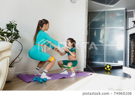 A young athletic mother and a girl do exercises together at home. Healthy development of parents and children, fitness and recreation. A young athletic mother and a girl do exercises together at home. Healthy development of parents and children, fitness and recreation. 74968106
