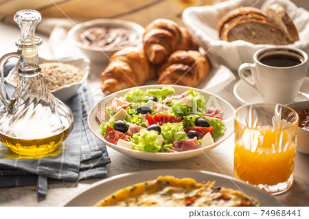 Broad assortment of food including omelette, croissants, salad, bread, oatmeal, jam, waffles, honey, choclate spread, coffee and orange juice served on a table 74968441