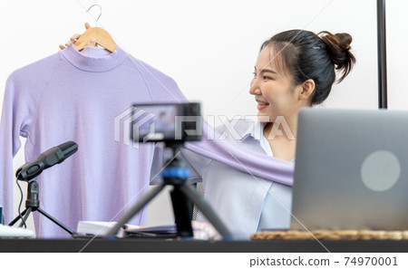 Young Asian women show off the clothes customers want to see through a live performance with a camera, Selling things through video recording or live shows via the Internet, Record live. Young Asian women show off the clothes customers want to see through a live performance with a camera, Selling things through video recording or live shows via the Internet, Record live. 74970001