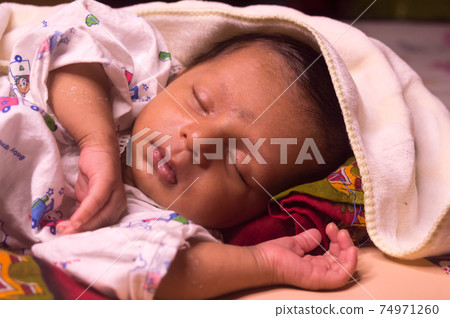 Close up face of cute sleeping newborn baby boy in drowsy eyes with sleepy mood. One month old Sweet infant toddler Closeup portrait. Indian ethnicity. Front view. Child care peace tranquil background Close up face of cute sleeping newborn baby boy in drowsy eyes with sleepy mood. One month old Sweet infant toddler Closeup portrait. Indian ethnicity. Front view. Child care peace tranquil background 74971260