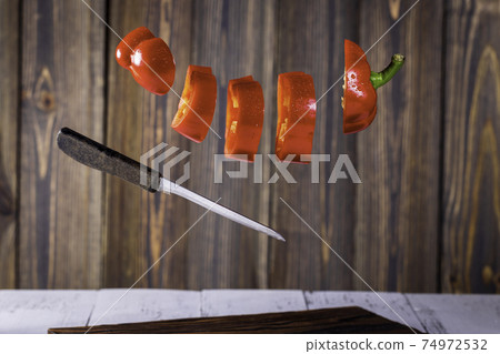 Sliced fresh red Pepper levitating.in wooden design kitchen. 74972532