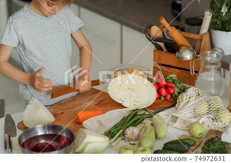 The child puts vegetables on the table and prepares a salad The child puts vegetables on the table and prepares a salad 74972631