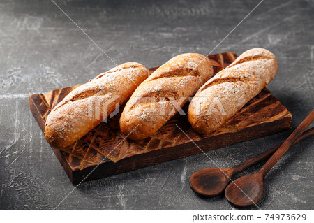 Three loafs of fresh baguette on gray background Three loafs of fresh baguette on gray background 74973629