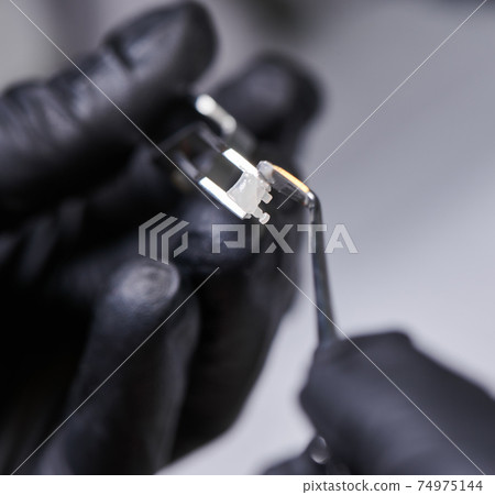 Steel dental forceps with ceramic bracket and a hand with a tiny colorful brush 74975144