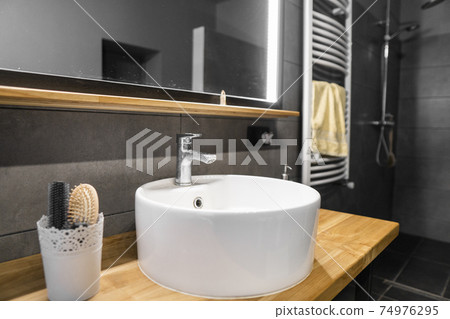 Bathroom interior with grey tile on a wall, stylish round sink and tap on a oak wood worktop. Minimalism in interior of bathroom. 74976295