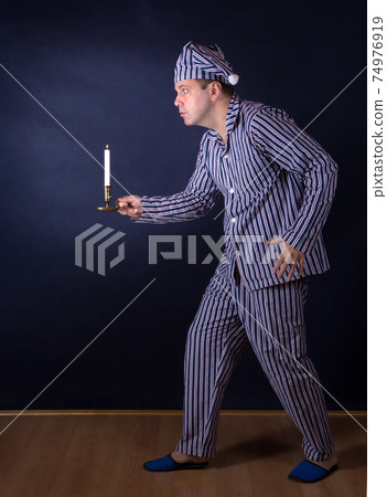 A frightened man with candle in pajamas 74976919