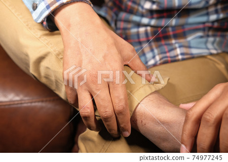 Close up on young man sitting on sofa suffering feet pain Close up on young man sitting on sofa suffering feet pain 74977245